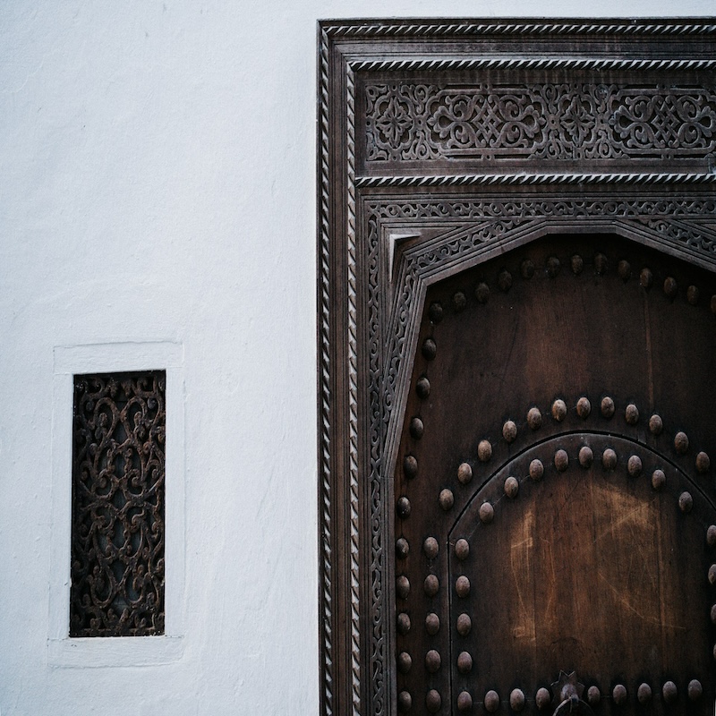 Ornate Moroccan interior with carved stucco arches, geometric patterns, detailed craftsmanship, and a richly decorated ceiling inside a grand architectural space