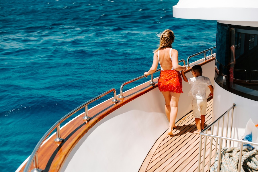 Person standing on the deck of a yacht overlooking bright blue ocean water.